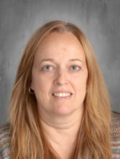 A woman with long hair wearing a cozy sweater, standing in a relaxed pose.