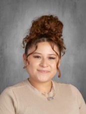 A woman with curly hair is wearing a cozy beige sweater with a warm smile.