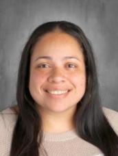 A woman with long hair wearing a white shirt, standing confidently against a neutral background.