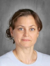 A woman with striking blue eyes wearing a crisp white shirt, exuding confidence and elegance.