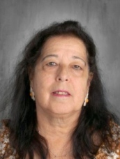 A senior woman with long hair dressed in a colorful floral shirt, radiating elegance and charm.