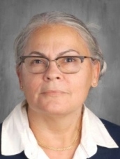 An older woman wearing glasses and a white shirt, smiling gently, exuding warmth and wisdom.
