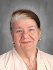 An older woman wearing a white shirt and a necklace, smiling gently at the camera.