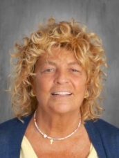 Portrait of a woman with curly blonde hair and a blue blouse against a gray background.