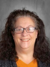 A woman wearing glasses and a black shirt, smiling confidently against a neutral background.